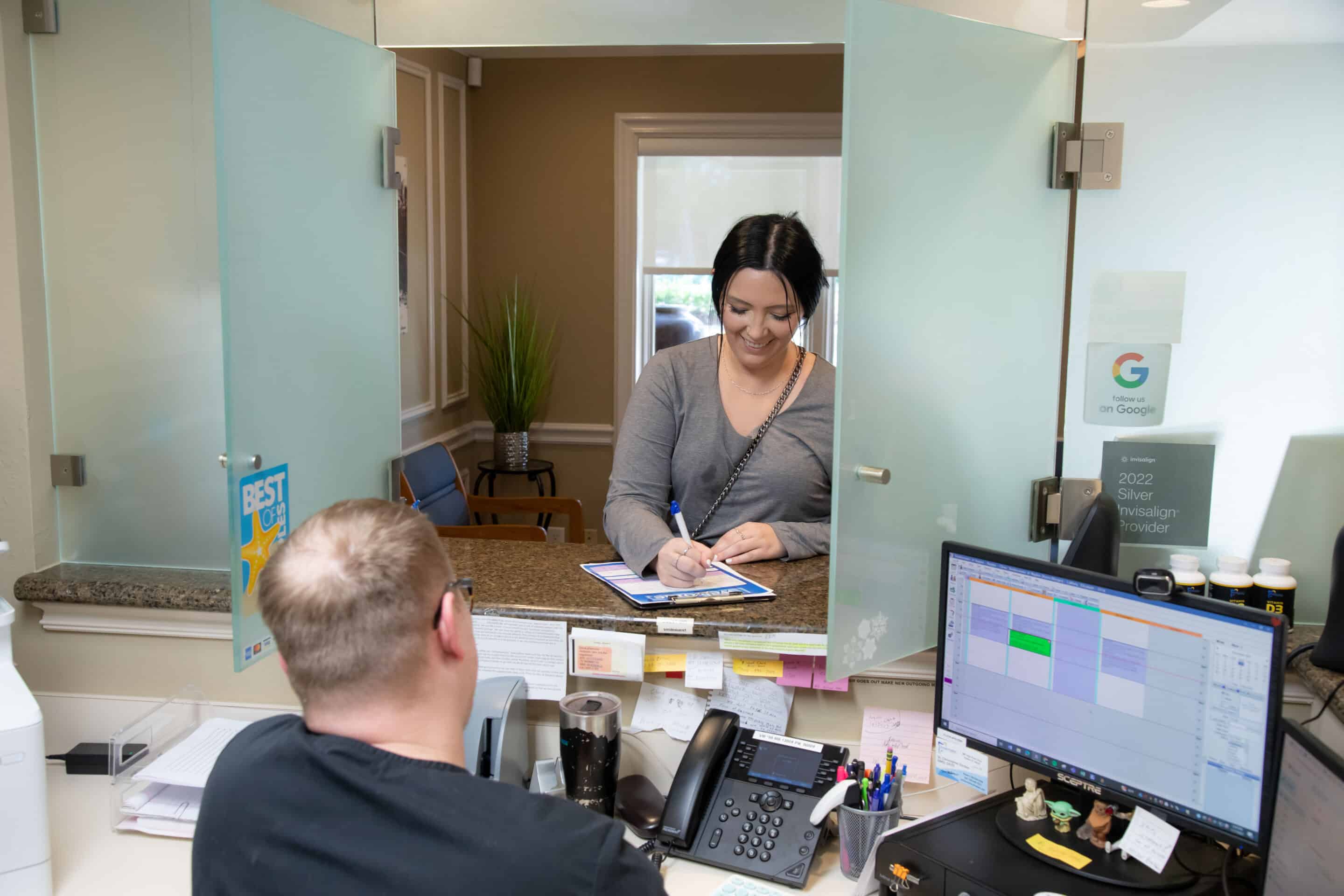 A patient fills out a form at the front desk of Smilecreator's Naples location while smiling.