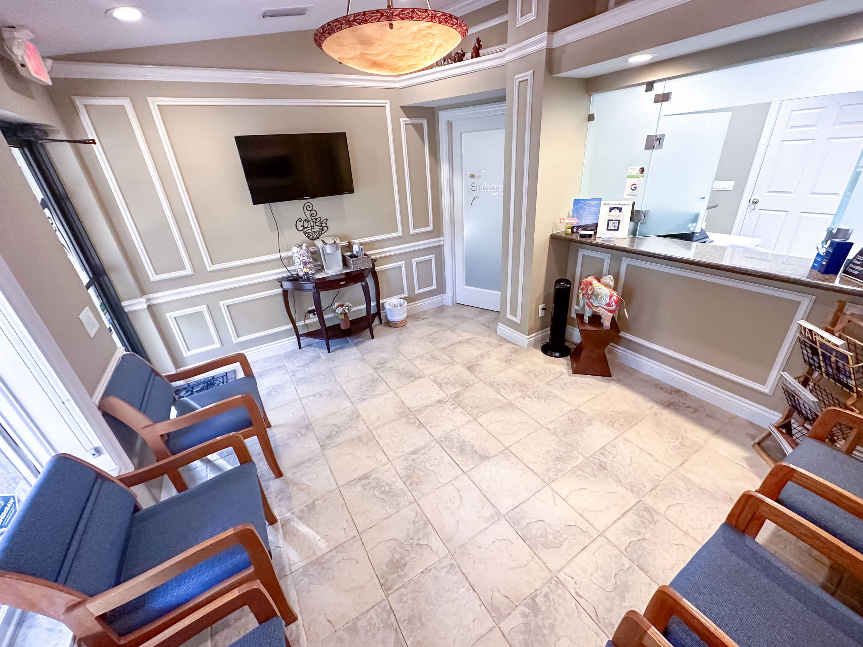 A view of the waiting room at Smilecreator's Naples location. Several cushioned chairs are arranged neatly, with a television and the front desk visible.